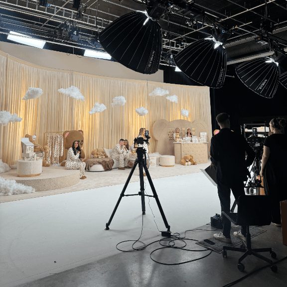The crew filming a baby-brand LIVE on a cream studio set dressed with clouds