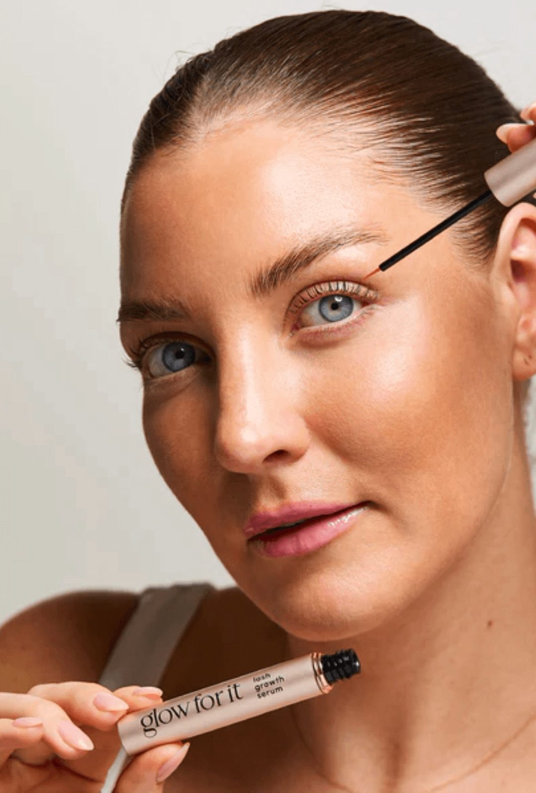 A close-up of a model's face as a Glow For It wand is brushed through her brow