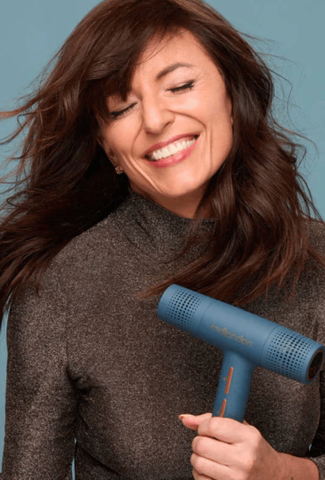 A model smiling mid blow-dry, holding the blue MDLondon hair dryer